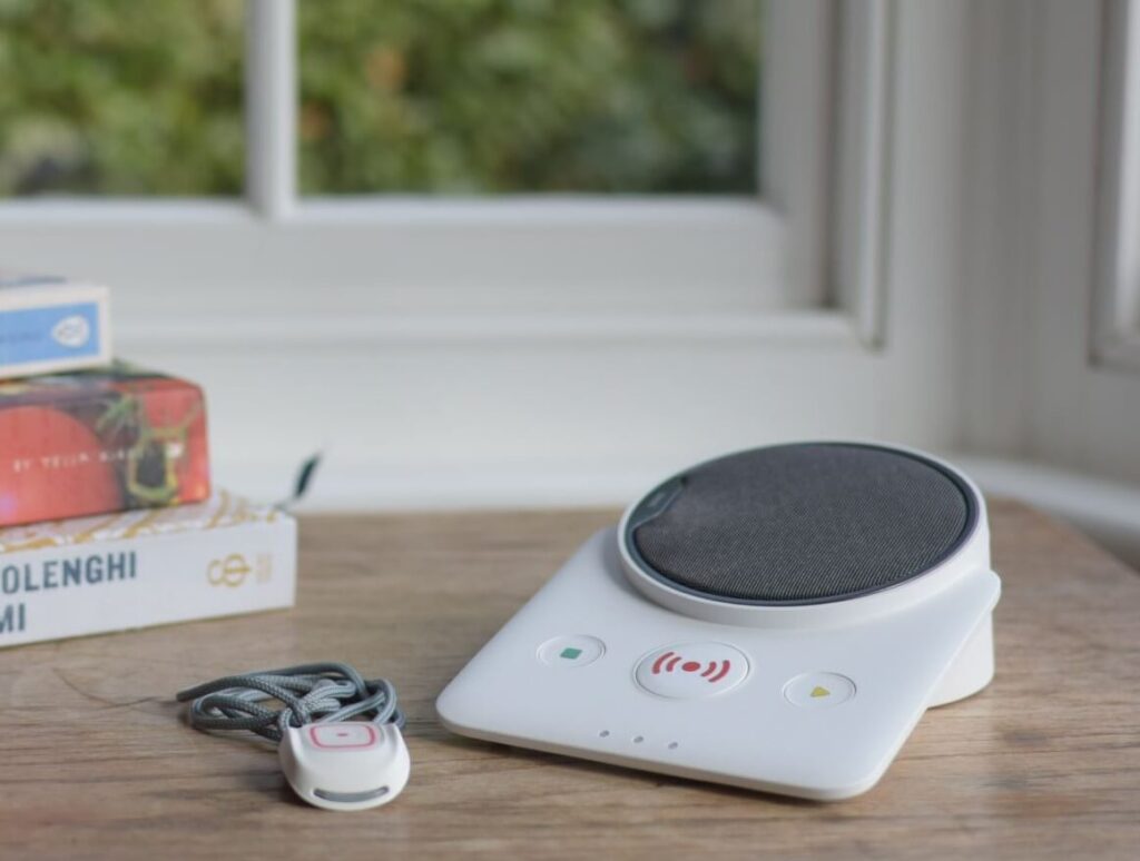 A personal alarm pendant and base unit on a side table